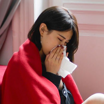 sick woman wiping her nose with a tissue