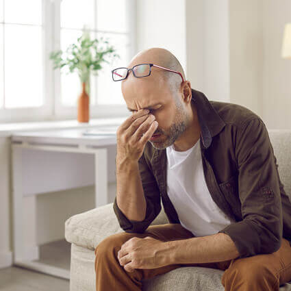 man pinching bridge of nose sitting in  living room