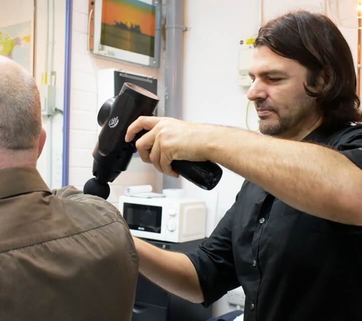 Dr Roddy Knight (chiropractor) using massage gun on patients shoulder