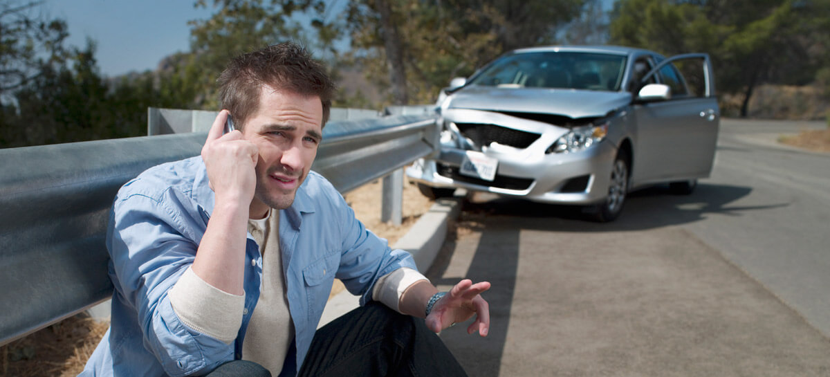 man sitting outside of car wreck