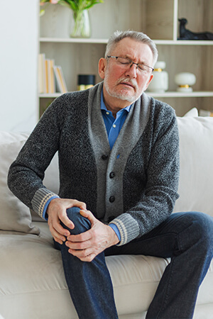 man sitting on couch holding knee in pain