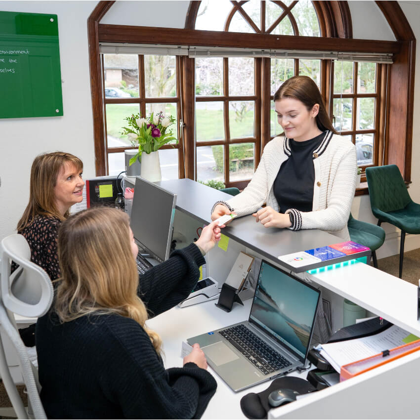 front desk team handing paper to woman