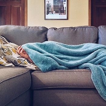 woman laying under blankets on a couch, sick