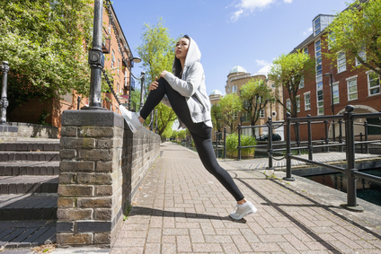 Full length side view of young fit woman stretching on sidewalk