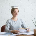 Portrait of attractive woman at desk, books on her head