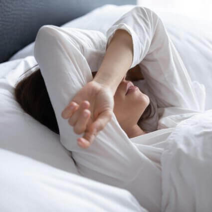 Woman lying in bed arms over eyes