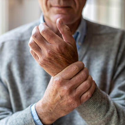 older-main-wearing-sweater-holding-painful-wrist-sq