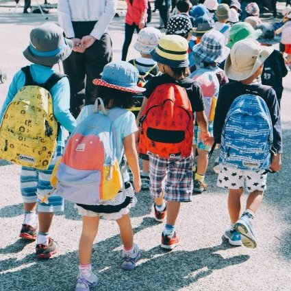 group of kids wearing white and orange backpacks walking on gray concrete pavement during daytime
