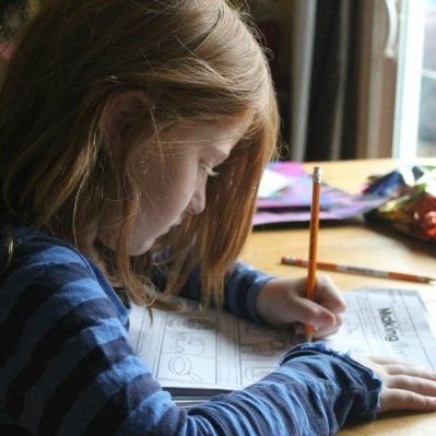 Young girl focused on homework at kitchen table with natural light.