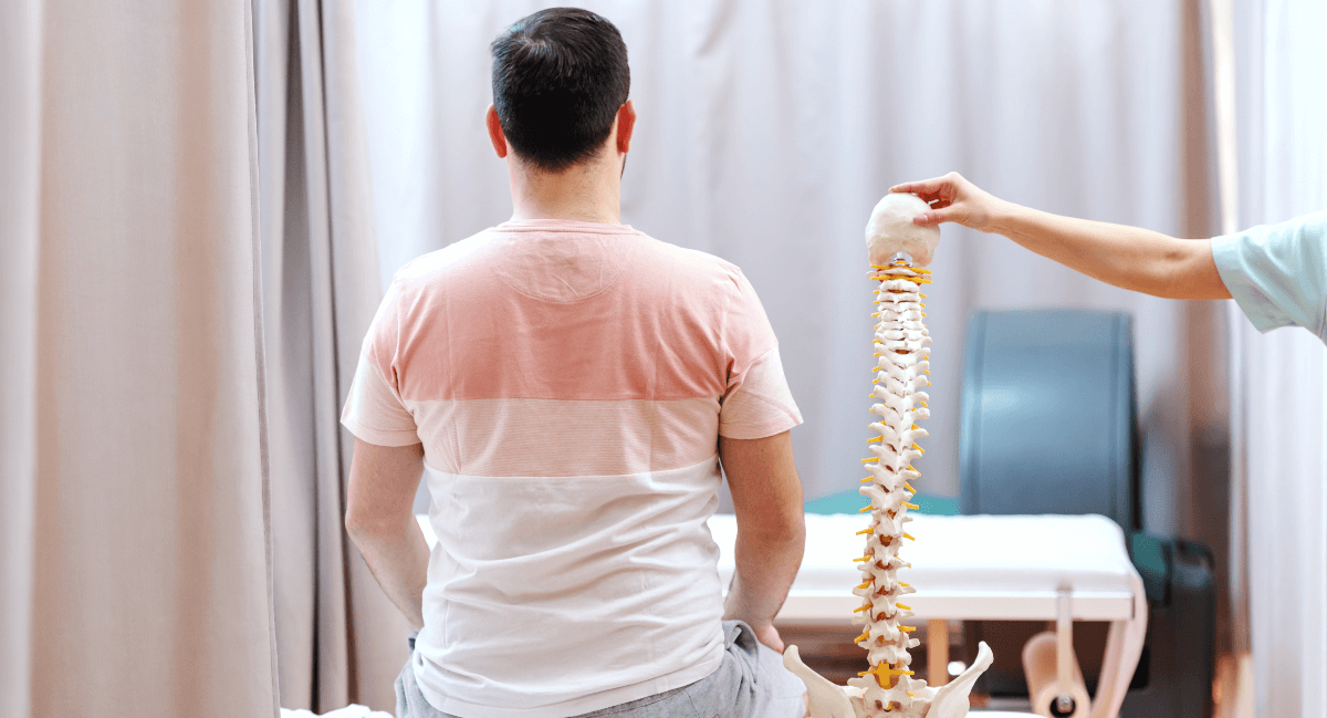 Male patient sitting next to a spine model