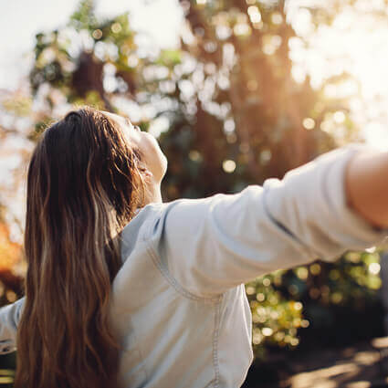 Woman looking up at sun with arms outstretched
