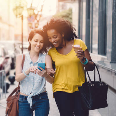 young women looking at a cell phone while walking