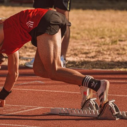 Athlete in red preparing to sprint on an outdoor track field. Focus on starting technique