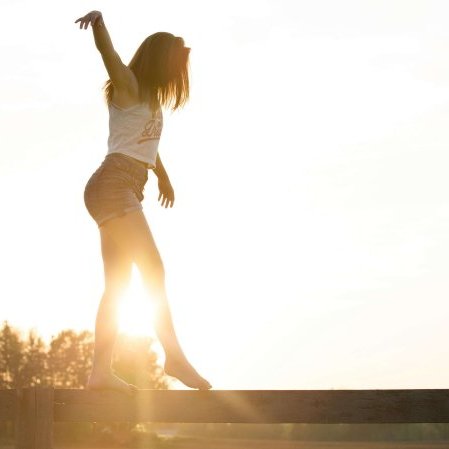A young woman balancing on a fence during a serene sunrise