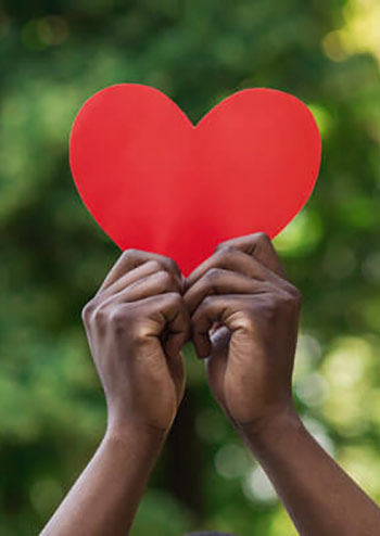 person holding a red paper heart shaped cutout