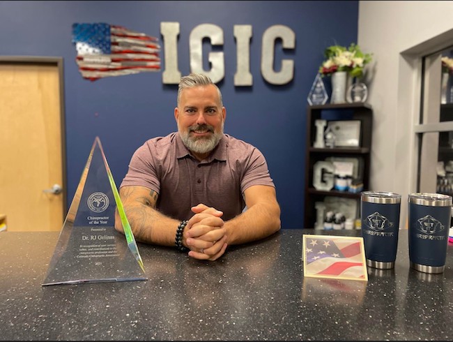 Dr RJ sitting at a desk with a pyramid shaped glass award that says he's 2020's Chiropractor of the Year from the Colorado Chiropractic Association