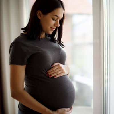 happy pregnant woman standing by a window
