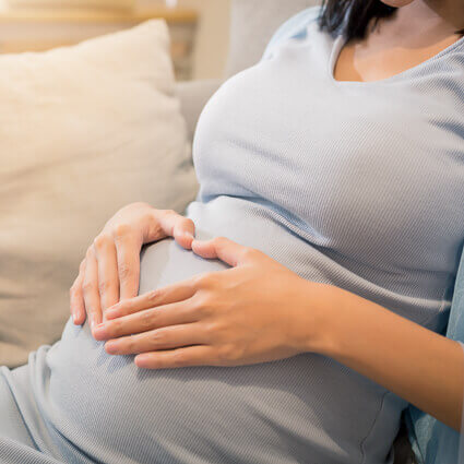 pregnant-woman-on-sofa-making-heart-sign-on-belly-sq