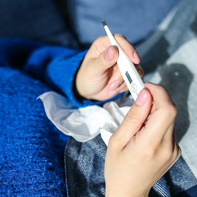 sick person laying down looking at a thermometer