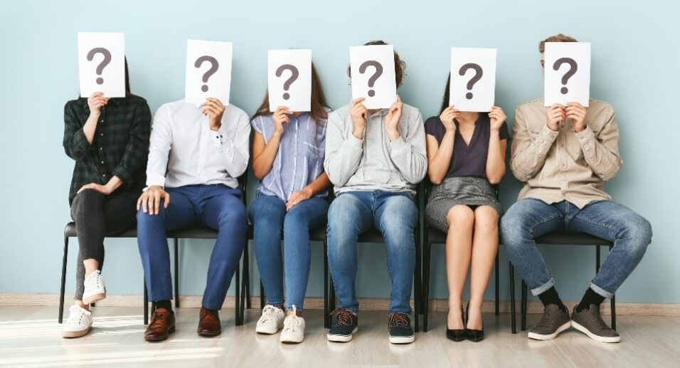 Patients in waiting room holding question mark signs up to their faces