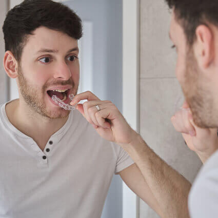 Man-Looking-in-the-mirror-holding-clear-aligner