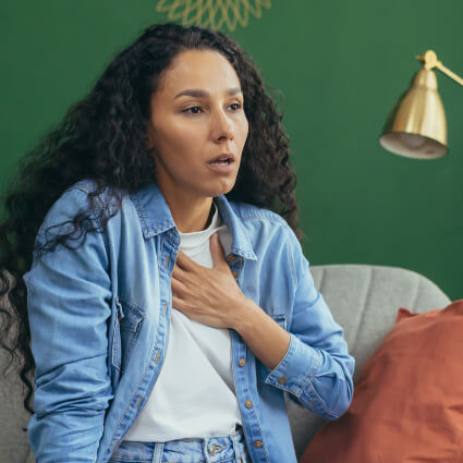 woman sitting on sofa with hand on chest