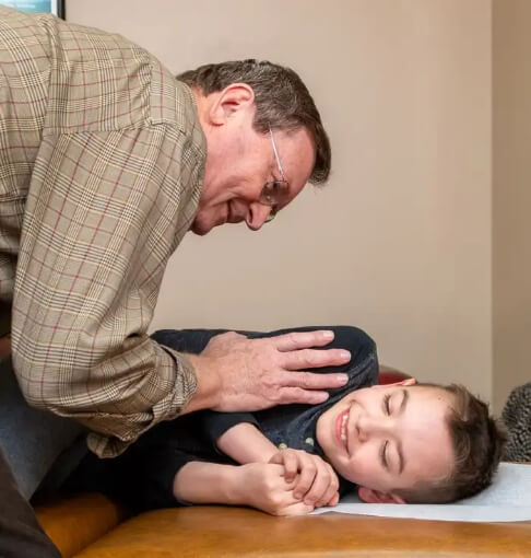 Dr. Pavel Bence providing a gentle chiropractic adjustment to a smiling child in Macomb, MI