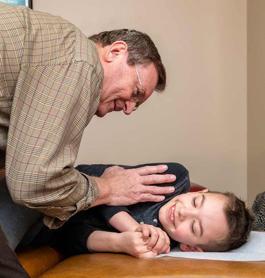 Dr. Pavel Bence providing a gentle chiropractic adjustment to a smiling child in Macomb, MI