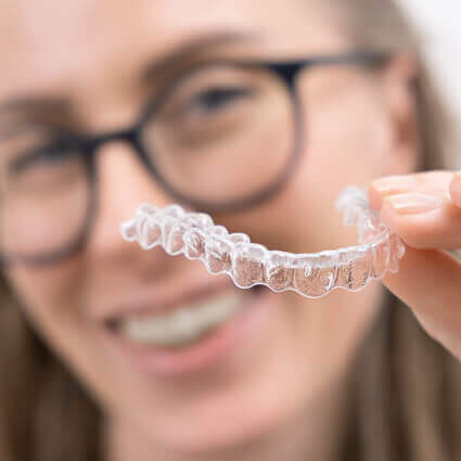 clear-aligner-with-woman-wearing-glasses-in-background-sq