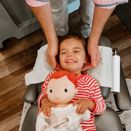 Dr. Jason adjusting a girl holding a doll