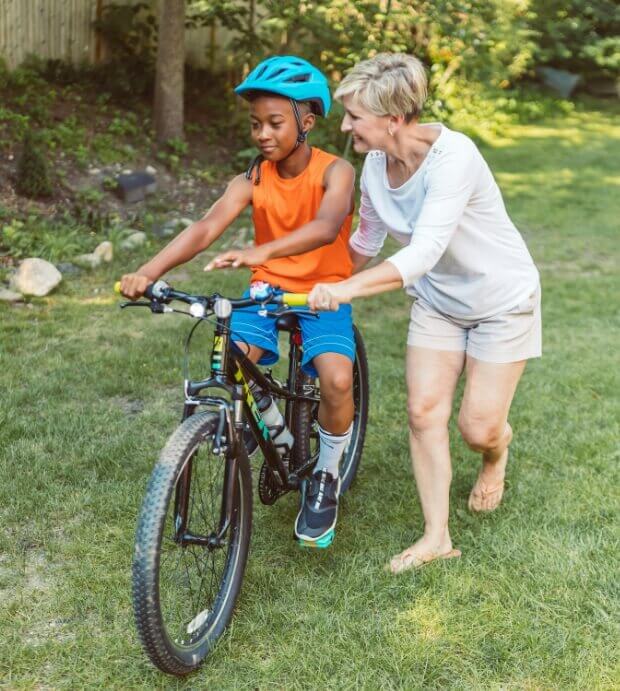 Woman assisting boy with riding his bike