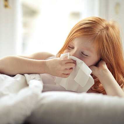 child blowing their nose in a tissue