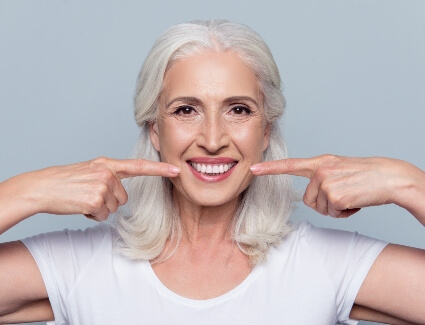 Older female smiling and pointing at mouth