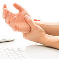 A man massaging his wrist in front of a keyboard.