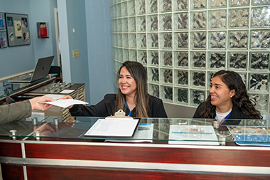 front desk staff smiling and handing forms to a patient