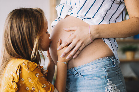 big sister kissing the pregnant belly of her mom