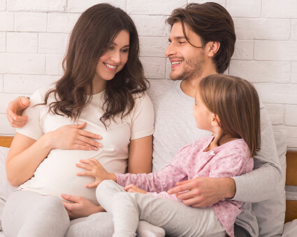 Pregnant mom on bed with husband and daughter
