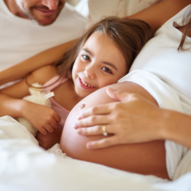 Little girl with head on mom's pregnant belly