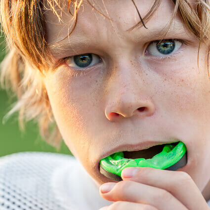 boy putting on green mouthguard
