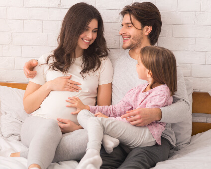 Pregnant lady on bed with husband and young daughter