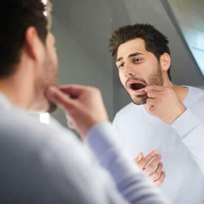 man looking at mouth in the mirror