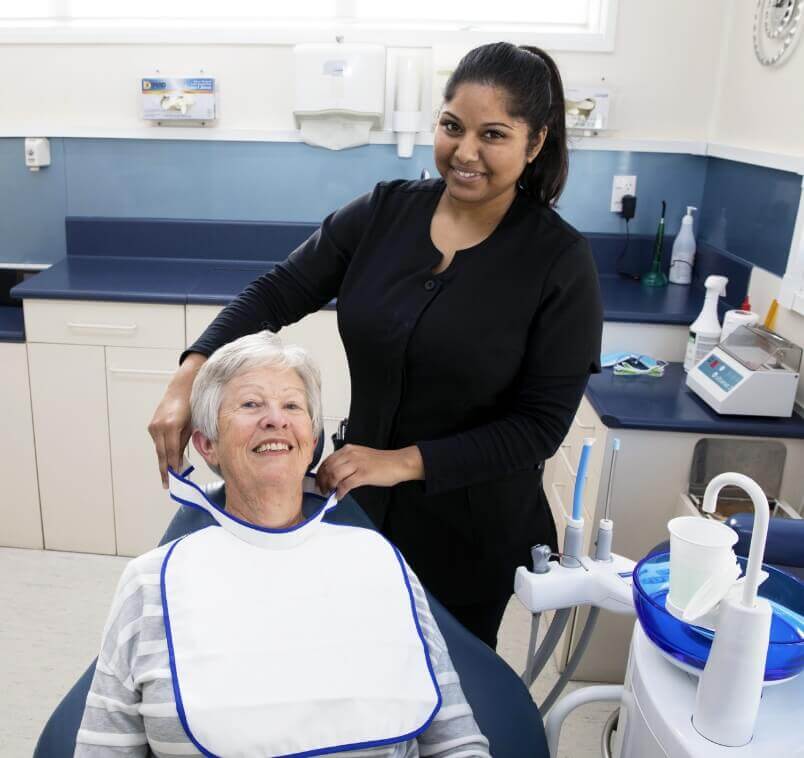 Blockhouse Bay Dental Centre team member putting bib on patient