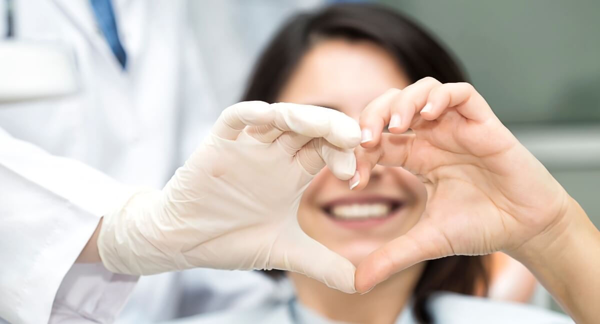 Woman and dentist making heart with hands