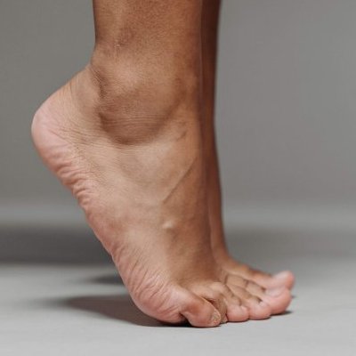 A minimalist close-up photo showing a bare foot standing on tiptoe on a grey surface.