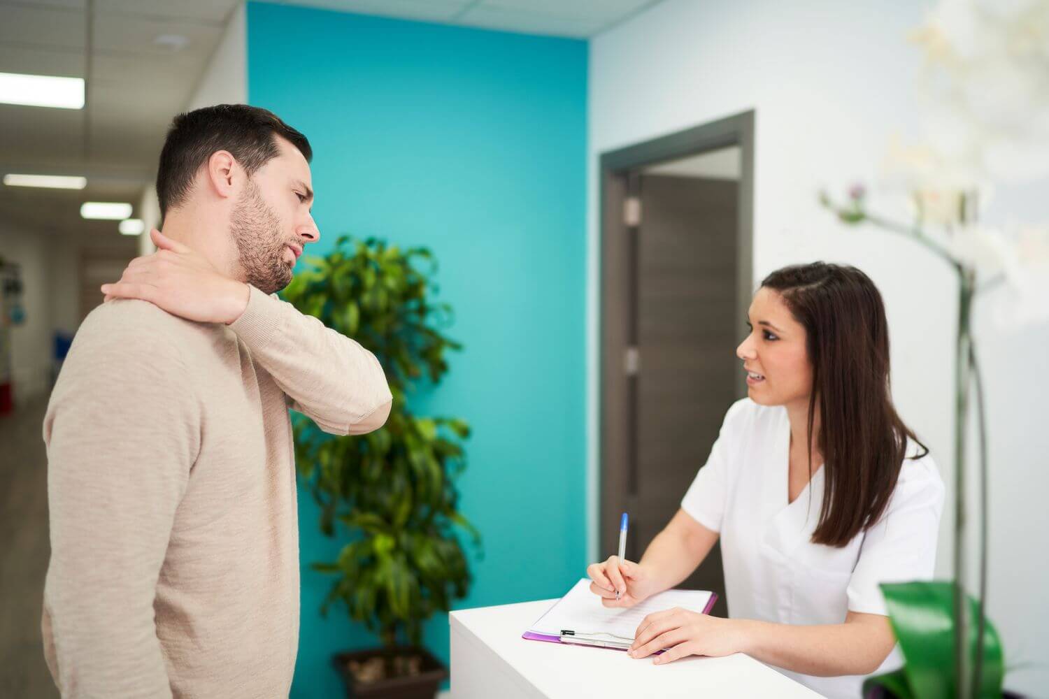 Man visiting chiropractor reception while holding neck