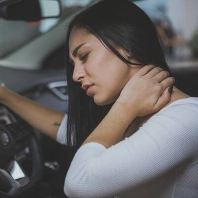 Beautiful young woman rubbing her neck, feeling sore after long drive. Female driver having terrible neck pain after whiplash injury in car crash. Healthcare, safety, pain concept