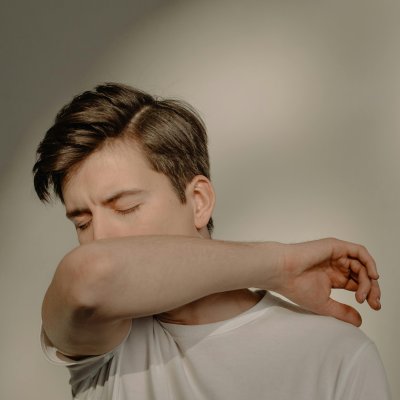 A young man sneezing into his elbow indoors, emphasizing health and hygiene.