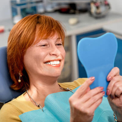 Woman admiring dental work in hand mirro