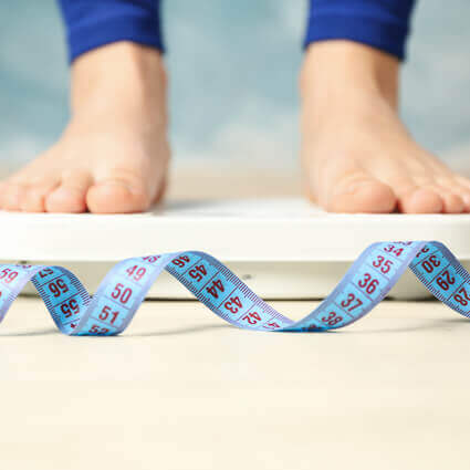 person-standing-on-scale-with-tape-measure-in-foreground-sq