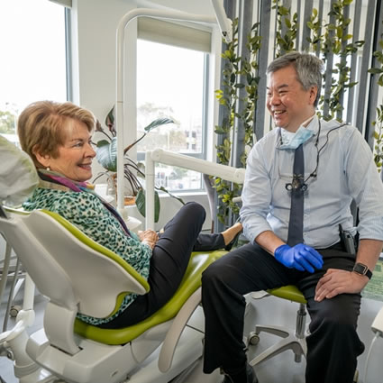 Dr Poe Lim sitting on a chair facing an older female patient sitting on a dental chair